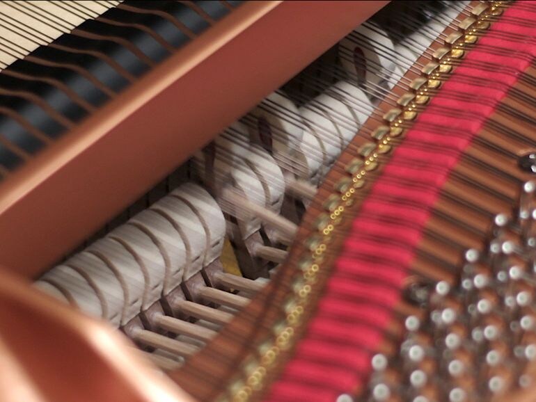 Photograph of a grand piano hammer striking strings