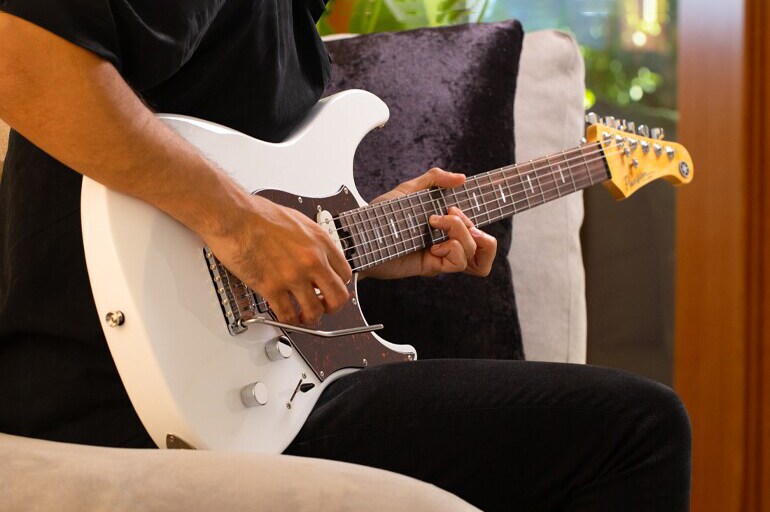 Closeup of male guitarist playing Shell White Pacifica Professional in home environment.