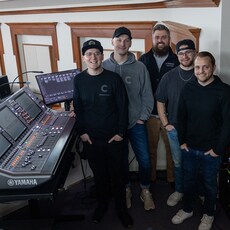 Members of the Christ Community Chapel audio team standing beside a Yamaha RIVAGE PM mixing console.