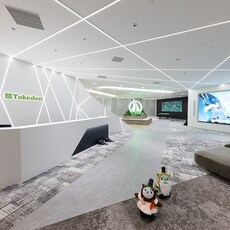 Image: Modern entrance space at TAKEDEN JP Tower Osaka office with linear ceiling lighting, large digital displays, and lounge seating